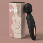 Carrie — czarny masażer wand z karbowaną główką i złotym panelem, obok pudełko gisty