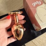 Dłoń z czerwonym manicure trzyma różowozłoty korek Elva L nad czarnym woreczkiem