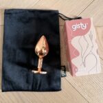Korek analny Elva M w kolorze rose gold na czarnym woreczku obok pudełka gisty