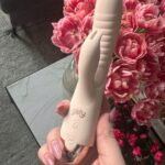 Dłoń z różowym manicure trzyma beżowego Bibi na tle różowych piwonii